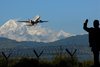 Kathmandu valley, Nepal: Tribhuvan International Airport - plane taking off with Himalayas behind - man waving outside razor wire fence - photo by J.Pemberton